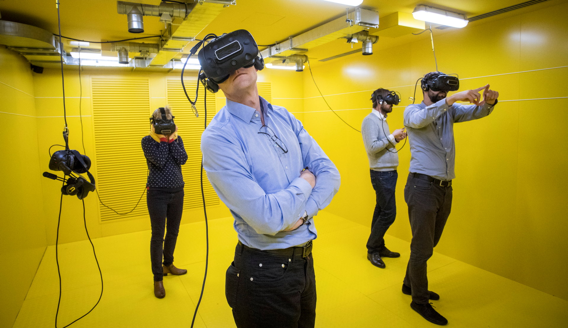 Vier Personen stehen in einem vollständig gelben Raum mit Virtual-Reality-Brillen auf dem Kopf.